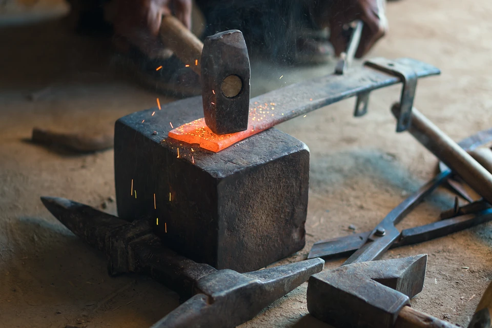 Atelier de forge intérieur, artisan manipulant une pièce métallique chauffée au rouge incandescent avec des pinces de forgeron